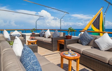Motor yacht Nita K II's aft deck with grey sofas and teak side tables 