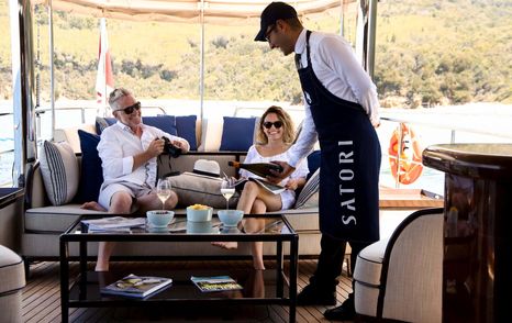 Male crew member pouring drink for two guests on sofa