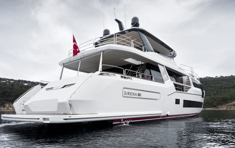 Aft water-level view of Sirena 88. Swim platform and exterior main deck area visible, with green foliage and elevated terrain in background.