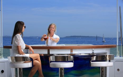 Crew making drinks at deck bar, sea in the background.