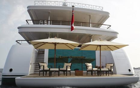 Aft view of Lady Christine with fold-out beach club terrace, teak deck, umbrellas, and seating arranged above the waterline.