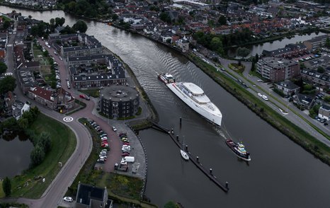 Aerial view of the Feadship superyacht Project 825 being escorted along a Dutch waterway.