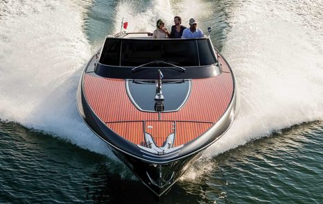 Classic tender with three guests in it viewed from front with spray emanating either side