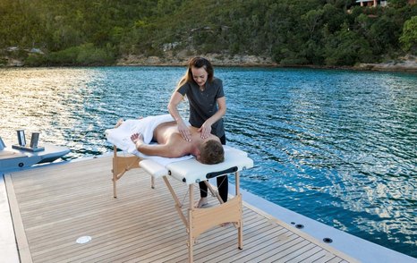 Masseuse massaging male guest on deck with water in background