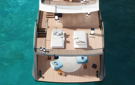 Aerial view looking down on Estrade superyacht, showing beach club on bottom deck and sun loungers on second deck with crystal clear water around the boat