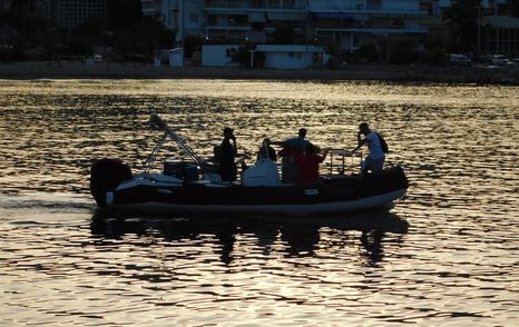 Workers on tender boat in early morning with coast and houses in the background