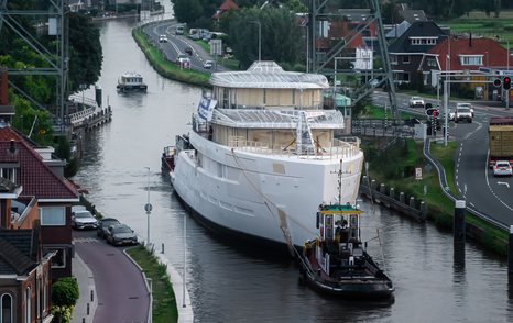 Feadship Project 825 underway on a Dutch waterway, with roads and houses either side.