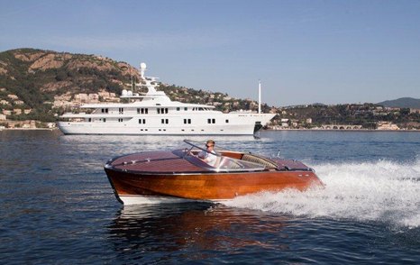 Classic tender boat moving at speed with superyacht and pictureque coast in the background