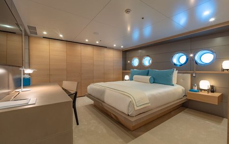 VIP cabin onboard superyacht WANDERLUST, central berth with porthole windows across the back, facing bureau and large mirror.