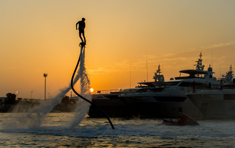 Man performing watersports demonstration at dusk during the Dubai International Boat Show. Superyachts moored in background.