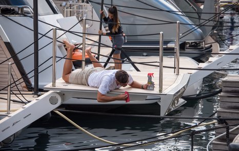 Man laying on a yacht swim platform cleaning the edges.