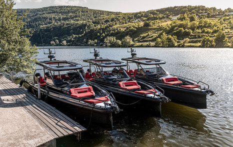 Three chase boats moored next to each other with trees on hills in background