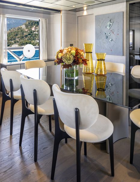 Dining area onboard Custom Line 140. Long glass table surrounded by eght cream chairs with autumnal floral bouquet centre.