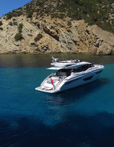 Princess S65 Mk2 at anchor in clear blue water beside a rocky coast