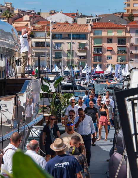 Overview of boardwalk at Cannes Yachting Festival with many visitors viewing superyachts on either side.