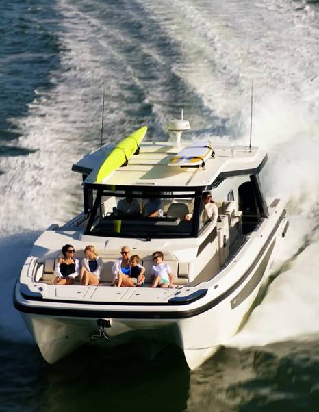 Aquila 45 Sport yacht cruising at speed with guests on forward seating, highlighting wide bow lounge and power catamaran stability