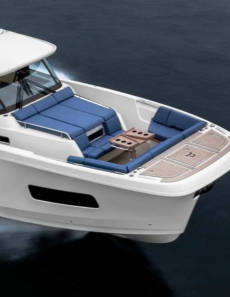 Foredeck lounge on the Aiata Sunfinder 50 with blue U-shaped seating, folding teak table and wide bow platform above the water.