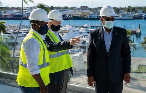 Bahamas Prime Minister Dr. Hubert Minnis tours Hurricane Hole Superyacht Marina at Paradise Landing, with two construction representatives. Moored superyachts in background.