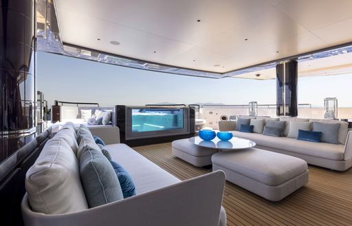 Aft deck onboard Superyacht POLESTAR, sofas facing inwards towards each other with a coffee table centre, pool visible towards aft of deck.