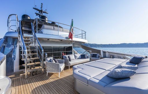 Exterior sunbathing area onboard Pershing 140 'Touch Me', large sunpads to starboard with rattan seating facing, surrounded by sea and land in distance