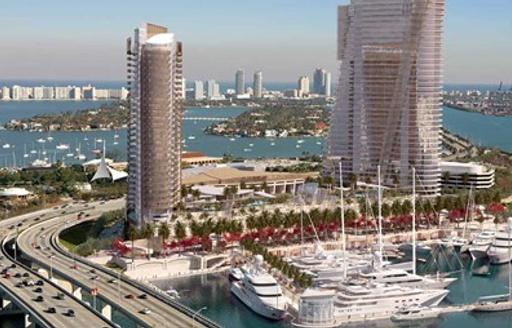 Close up image of Yacht Haven Grande Miami at Island Gardens, superyachts moored with two towering skyscrapers adjacent, surrounded by sea.