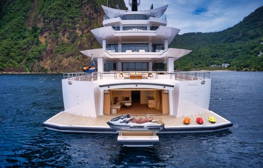 Overview of the beach club onboard superyacht ARTEFACT. Water toys lay on the swim platform, surrounded by elevated terrain.