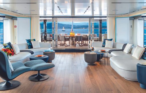 Upper salon onboard CRN RIO superyacht. Sofas sat facing against opposite walls with al fresco dining area visible in background.