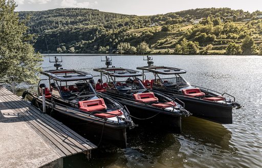 Three chase boats moored next to each other with trees on hills in background