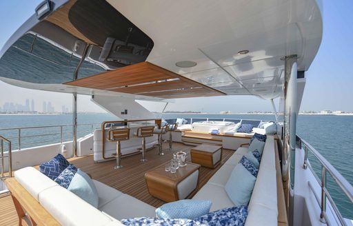 Overview of Majesty 120 sun deck, wet bar and stools to port side, with Jacuzzi forward and L shaped seating to starboard.