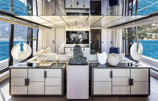 Upper salon onboard Custom Line 140. White block seating faces inwards. Superyacht surrounded by sea.