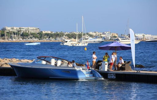 Sports boat berthed next to an exhibitor parasol, with the Bay of Cannes in the background.