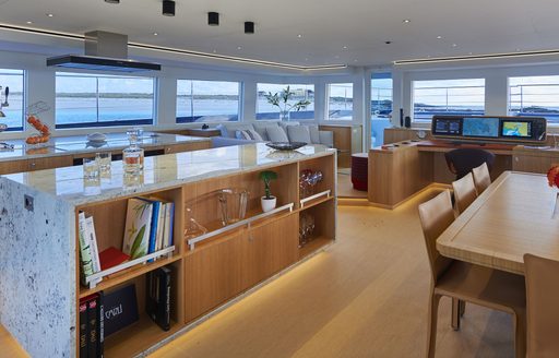 Main salon onboard Long Island 78 Power 4EVER. Dining table in foreground is joined by bookshelf and comfortable seating area in background next to helm station. Surrounded by lots of windows.