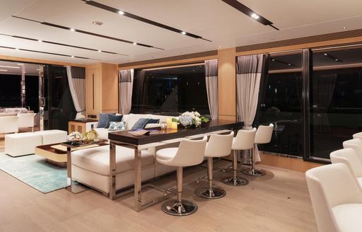 a dark wood-topped bar with four white bar stools sit between a seating area and dining table in the main salon of the FD87 Skyline