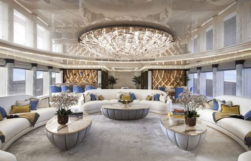 Overview of the main salon onboard superyacht Lady Jorgia. White curved sofas facing in with a large chandelier on the ceiling.