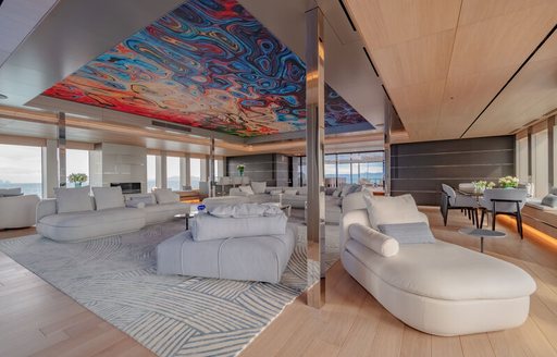 Side angle view of main salon onboard superyacht WANDERLUST. Cream chaise longue in foreground with additional cream coloured sofas and seats in background. 