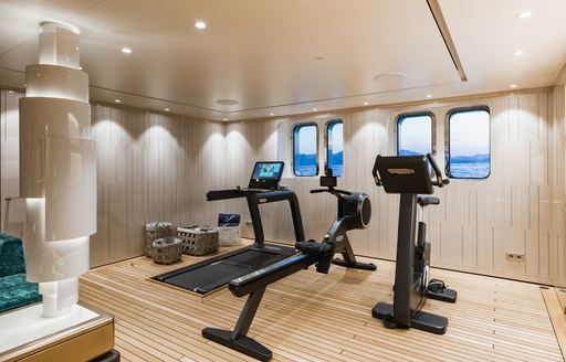 Overview of gym onboard superyacht SOARING. Row of gym equipment facing small windows looking over the sea.