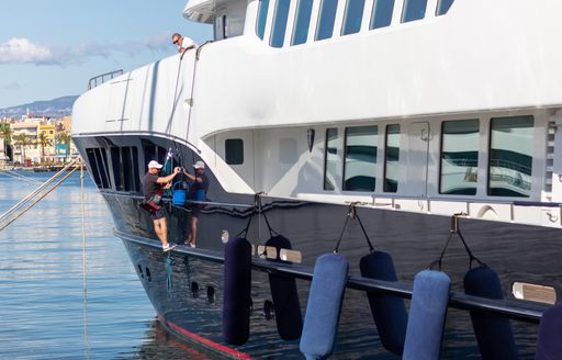 yacht crew in harness washing side decks of yacht