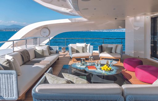 Overview of the aft deck onboard CRN RIO. White sofas around edges facing in to a low down coffee table. Sea visible in background.