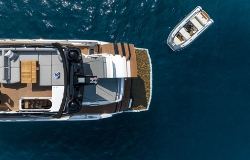 Aerial view looking down on Sunseeker 75 Sport Yacht, aft main deck visible with tender sat adjacent to yacht in the water.