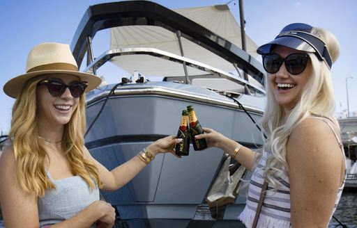 Two women posing in front of a motor yacht with champagne bottles