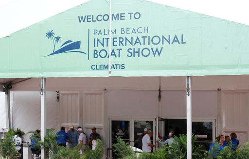 Large blue overhanging sign reading Palm Beach International Boat Show, groups of visitors relaxing on stools out front of cafe