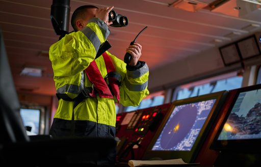 navigator wearing life jacket using binoculars and using vhf radio