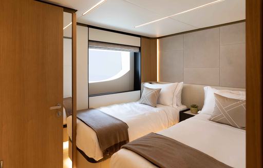 Overview of a twin cabin onboard the Majesty 111, two single beds on either side of a cabin with a door leading to an ensuite.