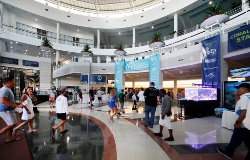 Interior of the Broward County Convention Center, exhibitor flags visible with some visitors walking around.