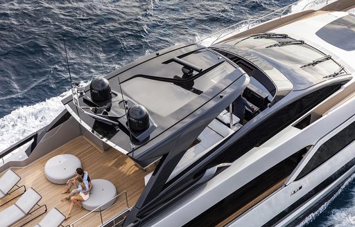 sundeck on board Argo 90 with man sitting down, sun pads, and glass hard top covering a seating area