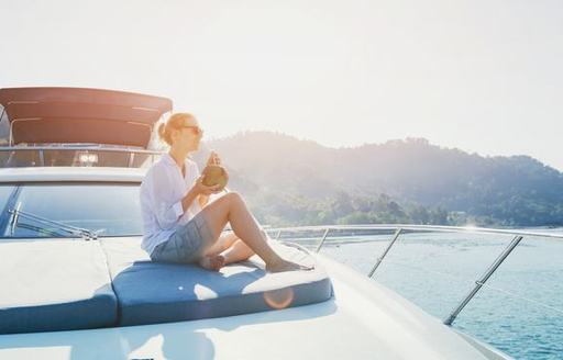 young female drinking on bow of motor cruising yacht