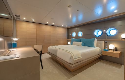 VIP cabin onboard superyacht WANDERLUST, central berth with porthole windows across the back, facing bureau and large mirror.