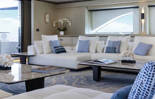 Main salon onboard superyacht ZAZOU, white seating with blue cushions facing low coffee table.