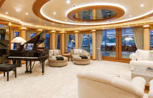 Grand piano in a lounge onboard Superyacht QUATTROELLE. Seating around the borders of the room with cream carpet and a black grand piano in the corner.