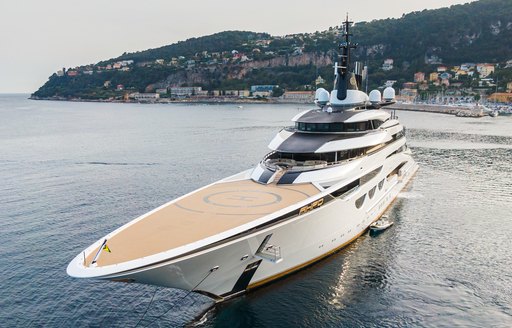 Frontal view of helipad on bow of megayacht AHPO, elevated terrain and buildings visible in far background.